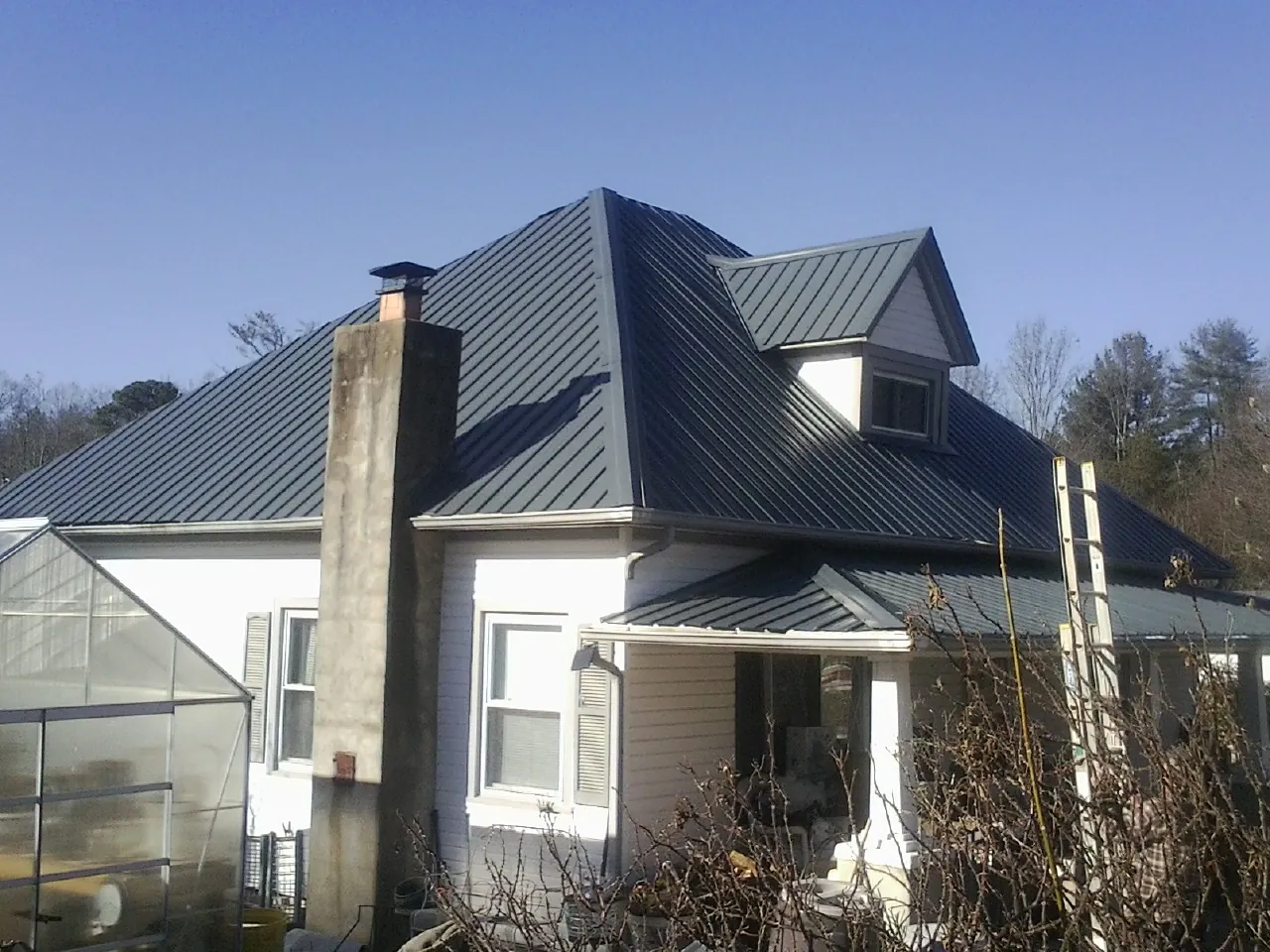 Dark blue standing seam metal roof on a white farmhouse with dormer — Slate & Tile Roof Repair by Roofing Brothers in Garden City