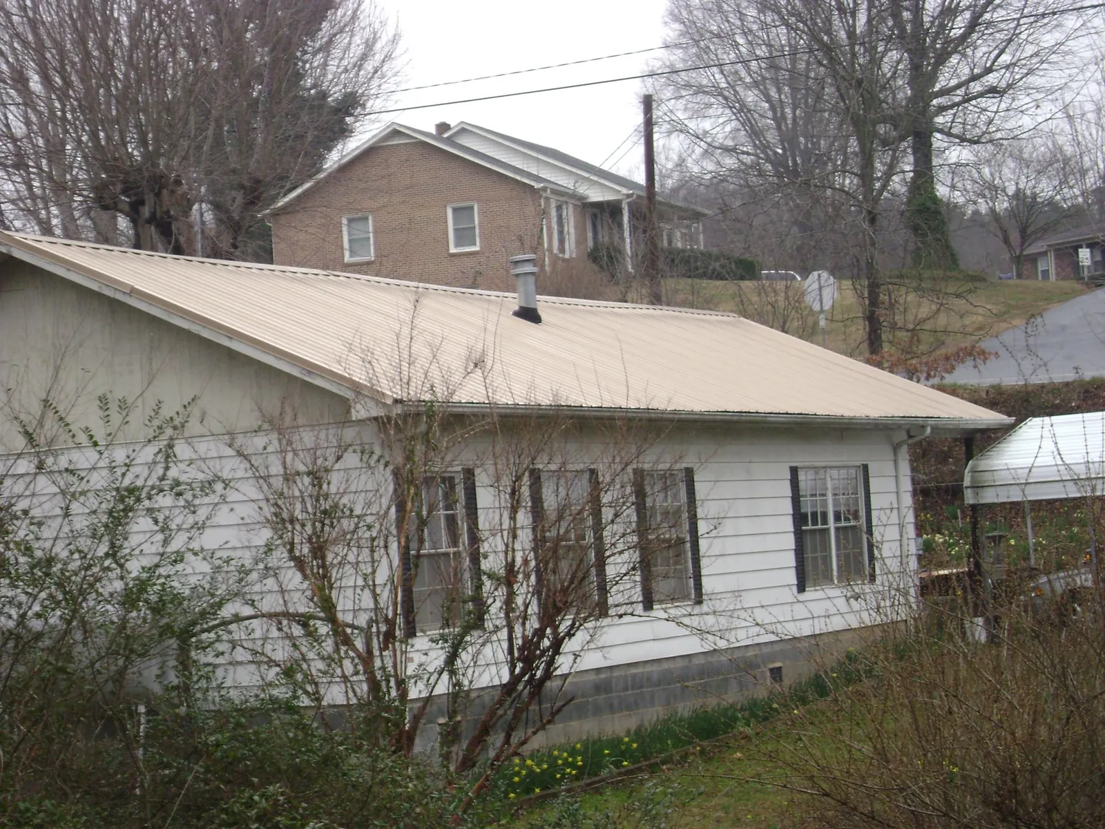 Tan metal roof on a white sided house set into a hillside — Commercial Roofing by Roofing Brothers in Garden City